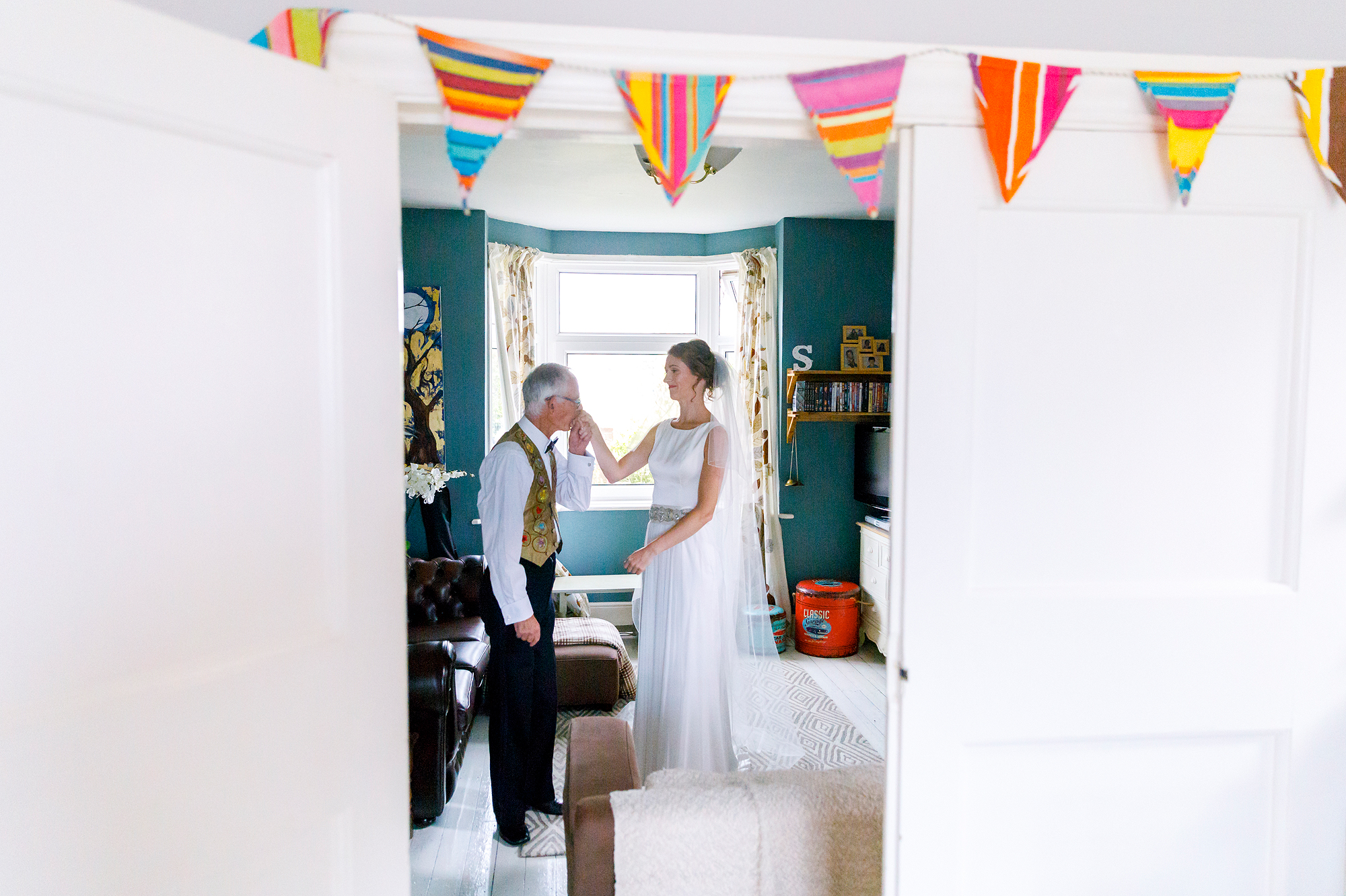 Woman in white dress with veil and older man in a waistcoat in decorated living room.