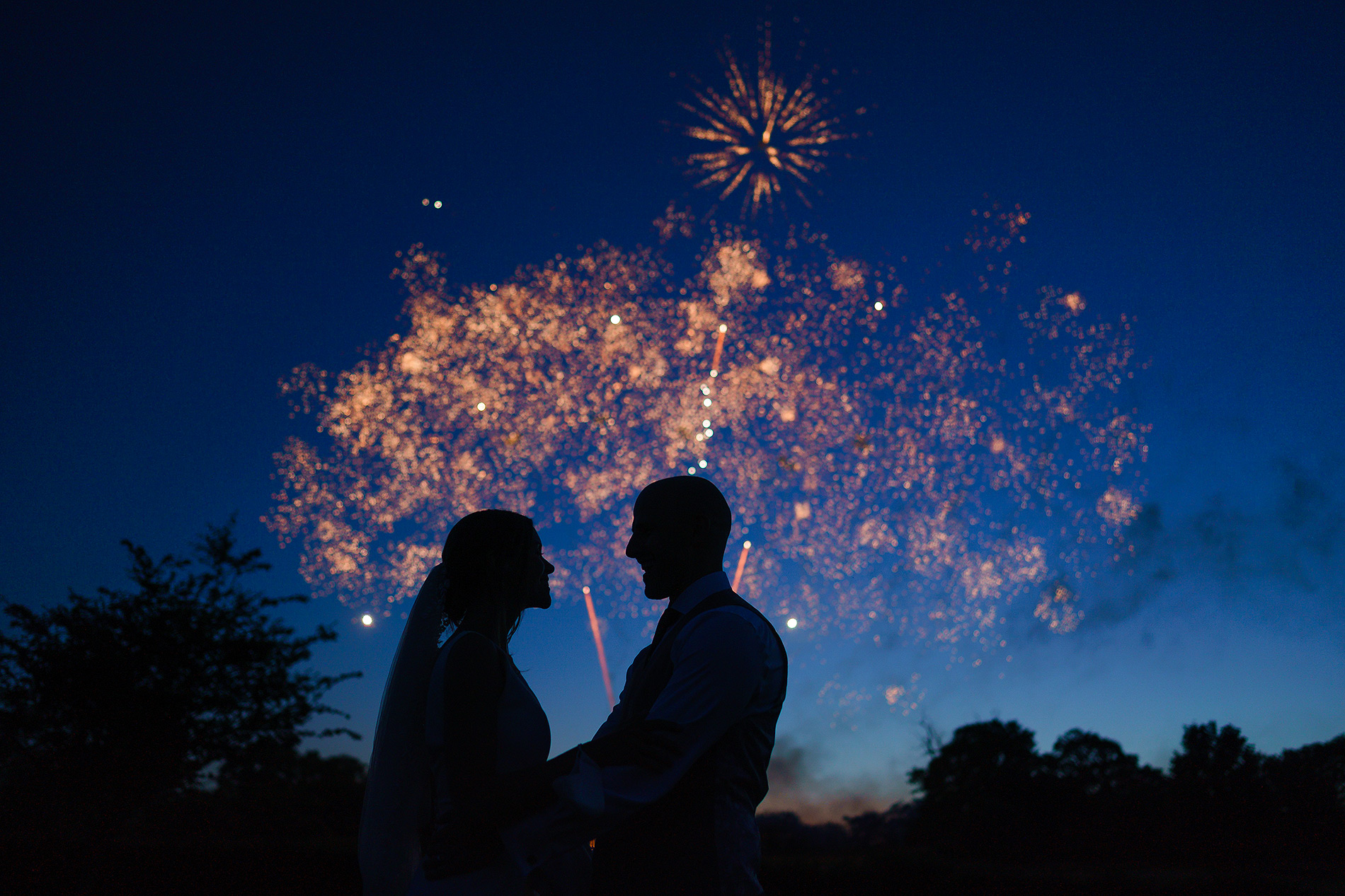 Couple silhouetted against vibrant fireworks lighting up the night sky.