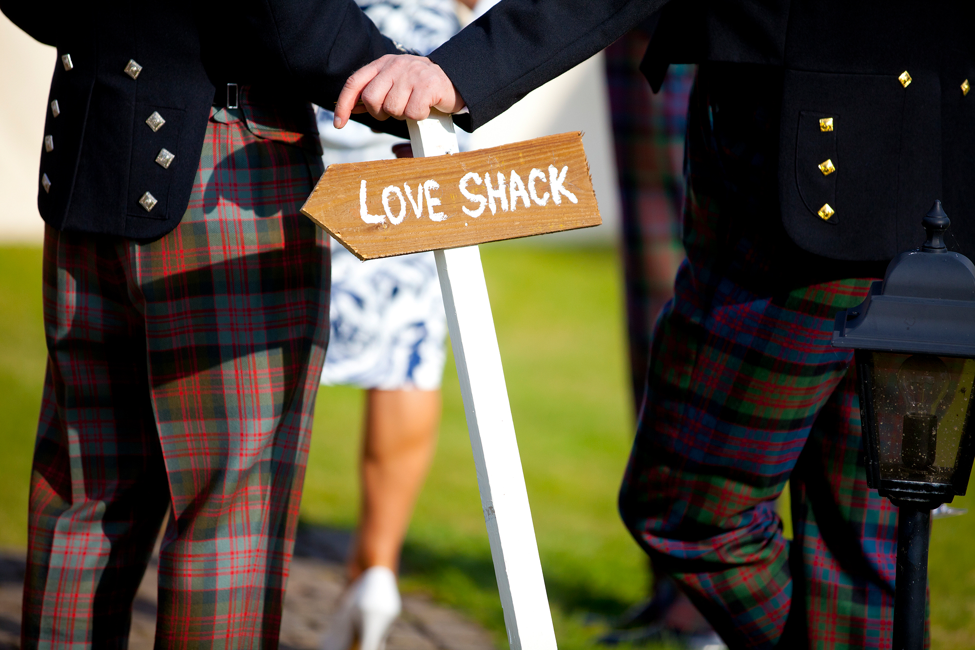 A group in tartan kilts stands by a "Love Shack" sign outdoors.