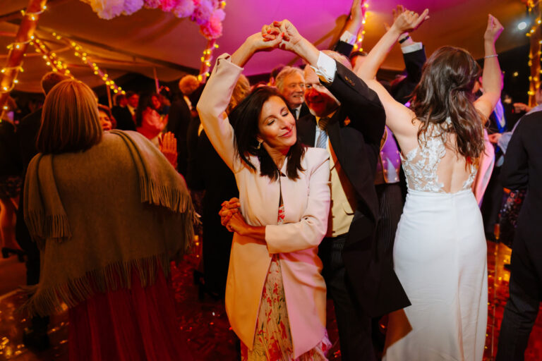 Indoor celebration with people dancing under string lights in formal and colourful attire.