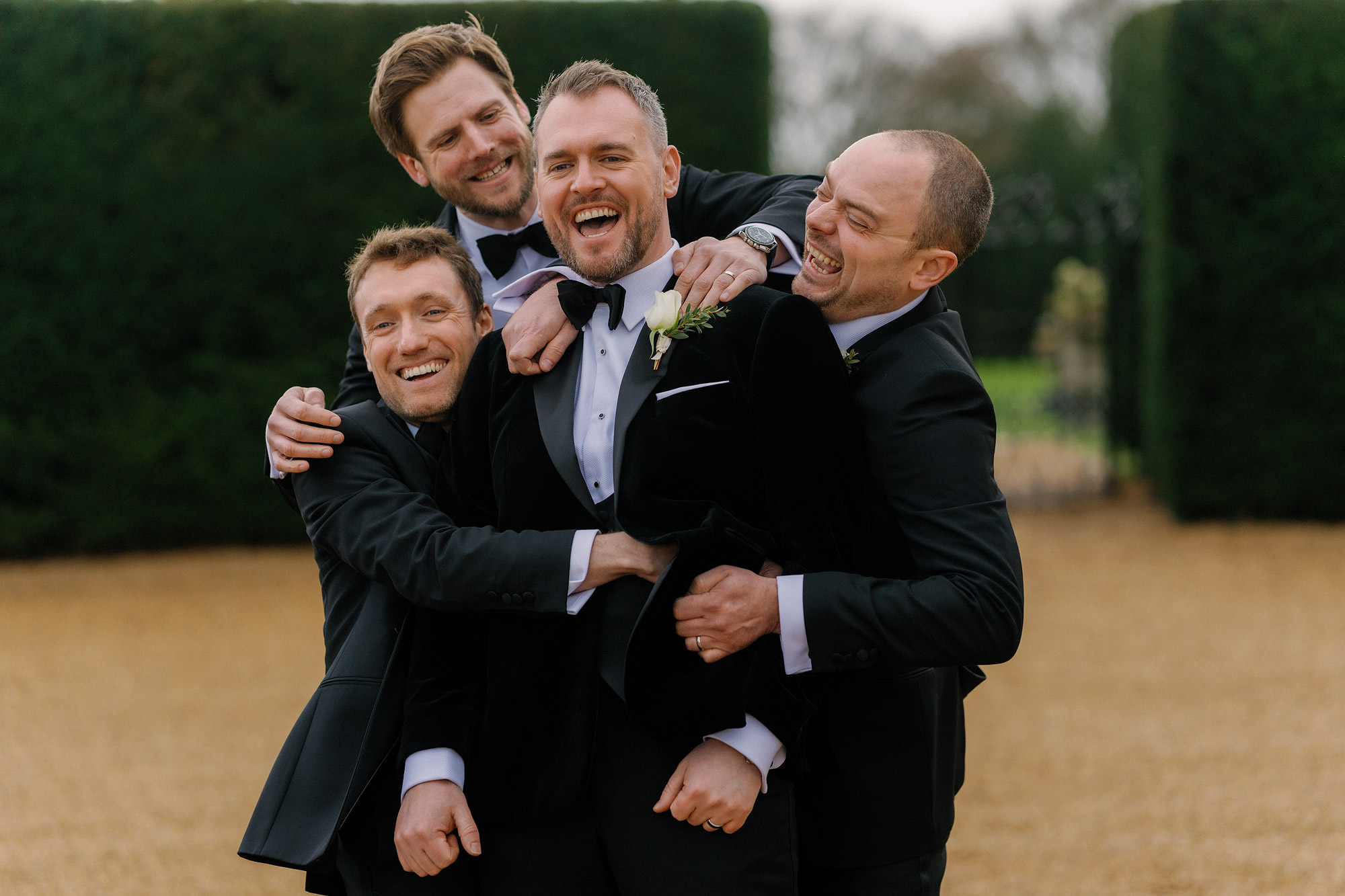 Four men in suits outdoors, smiling and embracing playfully.