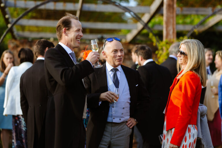 Group gathered outdoors at a formal event, with people conversing and holding glasses.
