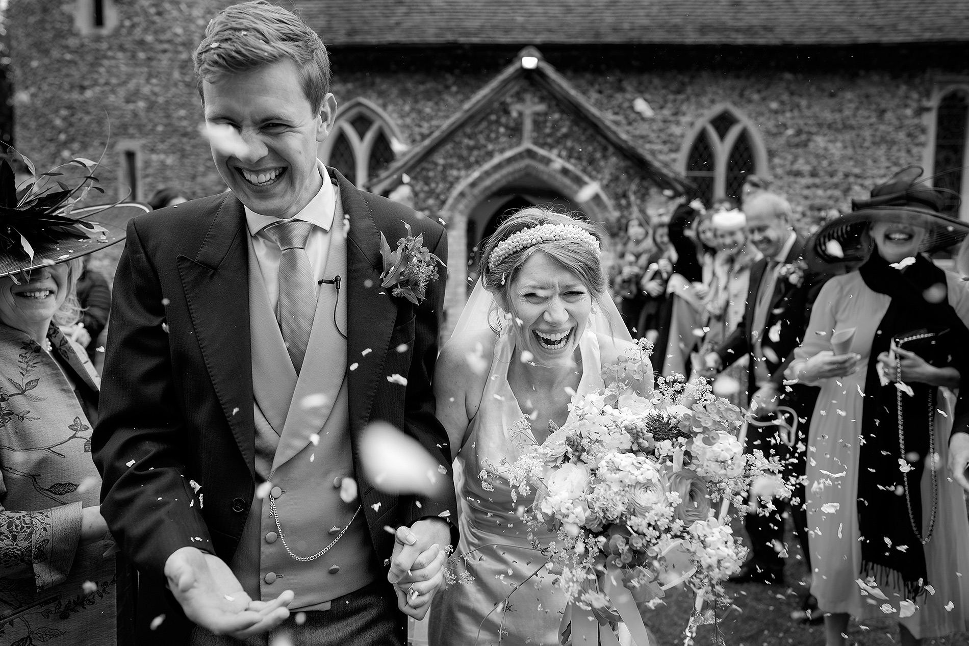 Couple exits church joyfully after wedding, surrounded by guests throwing confetti.