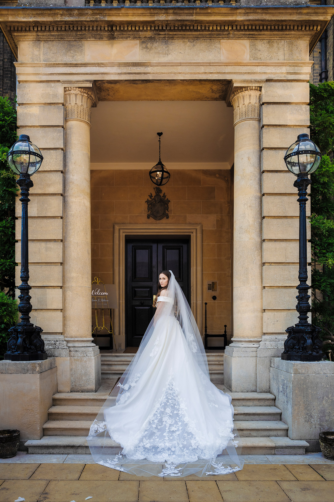 Person in a wedding dress at a historic stone building entrance with columns and lamp posts.